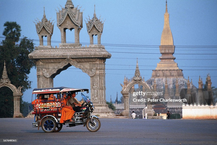 Chiếc xe tuk tuk chở các nhà sư đi ngang qua Pha That Luang, ngôi chùa lớn và nổi tiếng nhất thủ đô Vientiane, Lào năm 1991. Ảnh: Peter Charlesworth / LightRocket via Getty Images.