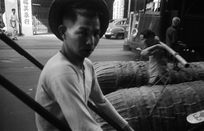 Anh kéo xe đi ngang qua một bà cụ bán sọt tre. Ảnh: Werner Bischof / Magnum Photos.