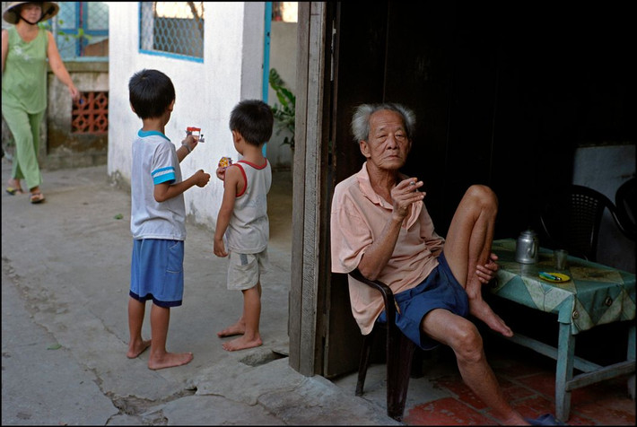 Cụ ông hút thuốc biên hiên nhà ở Phong Điền. Ảnh: Ian Berry/ Magnum Photos.