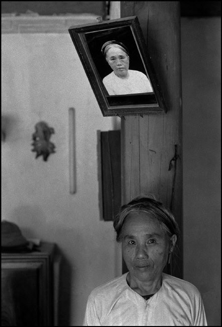 Cụ bà đứng dưới bức ảnh chân dung của mình. Ảnh: Ferdinando Scianna/ Magnum Photos.