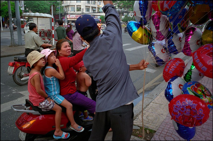 Bà mẹ dừng xe bên đường mua bóng bay cho ba đứa con ngồi trên xe máy. Ảnh: Ian Berry/ Magnum Photos.