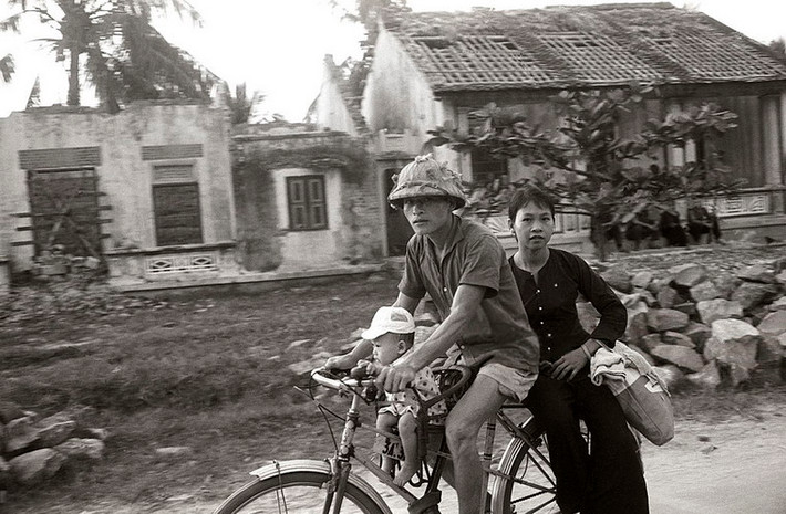 Hai vợ chống và đứa con đạp xe qua một khu dân cư bị Mỹ ném bom, miền Bắc Việt Nam 1965.