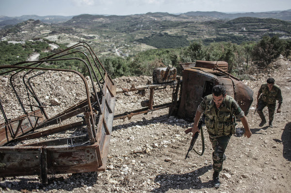 Các binh sĩ Syria đi tuần tra qua một chiếc xe tải han gỉ.