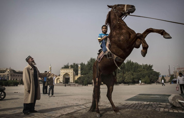 Cậu bé người Duy Ngô Nhĩ ngồi trên lưng ngựa trước nhà thờ Id Kah ở Kashgar.
