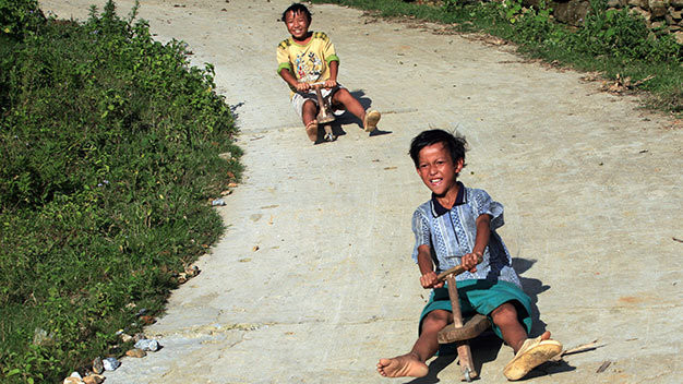 Hai em Sùng A Chung và Chàng A Ký 13 tuổi, dân tộc Mông, ở bản Hòa Sú Pản 1, xã Xứ Pán, Sa Pa (Lào Cai) thả dốc “chiếc xe máy” bằng gỗ - Ảnh: Lê Bích .