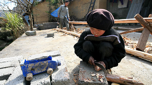 Em bé dân tộc ở bản Sủng Là (Hà Giang) cắt khoanh gỗ tròn để làm bánh xe cho chiếc ôtô từ bình nhựa đựng dầu xe máy bỏ đi - Ảnh: Lê Bích.