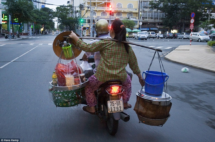Một phụ nữ gánh hàng khi cô ngồi sau một chiếc xe máy đi trên đường phố.