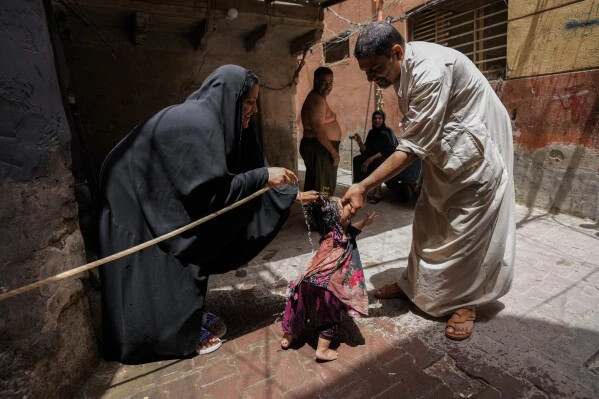 Người lớn xịt nước cho các con của mình bên ngoài nhà ở khu phố al Fadhil ở Baghdad, Iraq