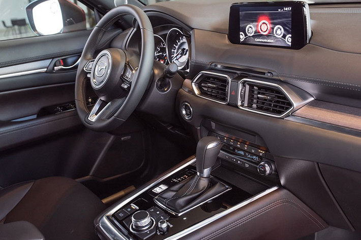 Bên trong nội thất, Mazda CX-8 sử dụng chất liệu da thuộc Nappa cho cảm giác mềm mại và mịn màng. Chất liệu gỗ tự nhiên được sử dụng để trang trí táp lô và cánh cửa xe. Vô-lăng gần như giống hệt CX-5. Nếu để ý kỹ, có thể thấy một chút khác biệt ở nút bấm Cruise Control tự động bám theo xe phía trước.