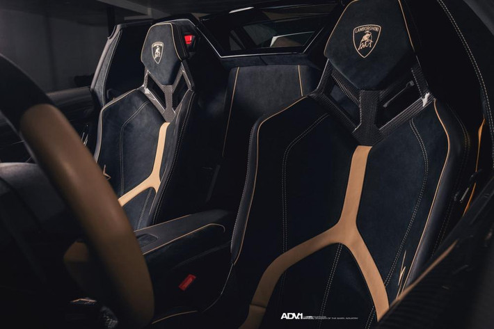 Tiến vào bên trong khoang lái chiếc siêu xe Lamborghini Aventador SV Roadster có "nội y" màu đen với điểm nhấn như chữ Y nằm ngược trên lưng ghế hoàn thành với màu vàng đồng tương tự như ngoại thất.