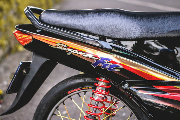 Giảm xóc sau Racing boy cho độ nhún êm ái hơn cũng như tăng độ cứng cáp cho xe với lò xo màu đỏ nổi bật cùng với lốp mới bánh căm. Cỗ máy 110cc trên chiếc xe máy Honda Wave cũ này vẫn được giữ nguyên bản, chỉ dọn lại và trang trí thêm một số chi tiết ơpr ốp ngoài.
