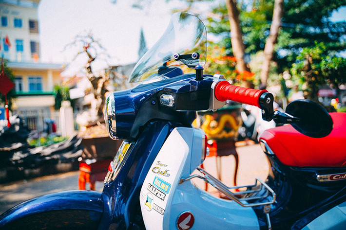 Để lấp đầy khoảng trống phần đầu xe do thiết kế quá nhỏ bé cuả Super Cub C125, chủ xe đã trang bị kính chắn gió Asahi xuất xứ từ Japan, vừa tăng độ thẩm mỹ mà còn cản gió tốt hơn. Cánh trái được trang bị kính gù CNC Racing siêu nhỏ gọn, khả năng nhìn về sau cũng đáp ứng tốt nhưng góc nhìn thực sự khá hẹp, chỉ thích hợp đi kiểng.