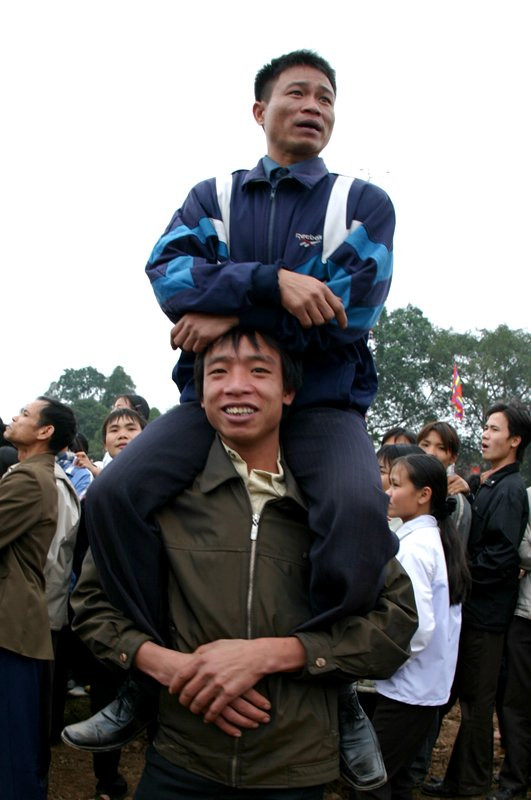 Hai người đàn ông thay phiên ngồi lên vai nhau để xem màn cướp phết trong lễ hội phết Hiền Quan, huyện Tam Nông, tỉnh Phú Thọ.