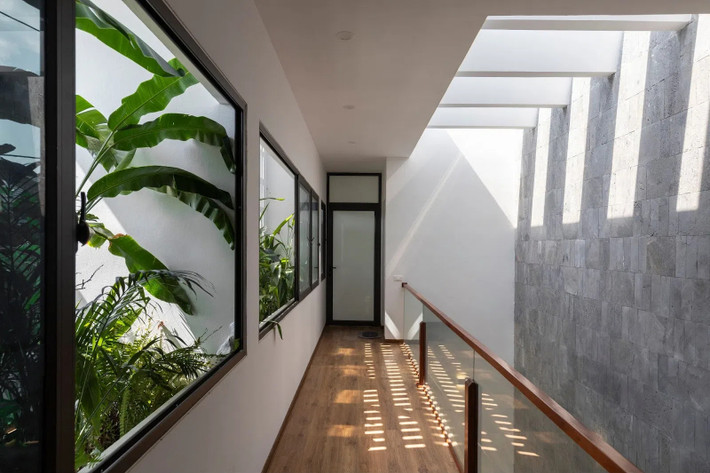 Tầng 2 và tầng 3 thông nhau bằng cầu thang mở, tận dụng tối đa ánh sáng từ giếng trời. Các cửa sổ hành lang tiếp xúc với môi trường được thiết kế tường gạch thông gió và cây xanh giúp giảm nhiệt độ, đảm bảo thông gió bên trong ngôi nhà. Nguồn ảnh: Nhật Hà, Phạm Quốc Huy