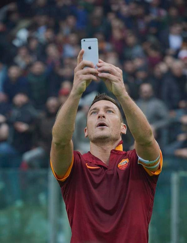 Để tri ân NHM của thành Roma và bắt kịp thời đại check-in, đội trưởng Francesco Totti đã cầm điện thoại của vị trợ lý và quay về phía khán giả để chụp ảnh tượng sướng. Ảnh: Goal.com