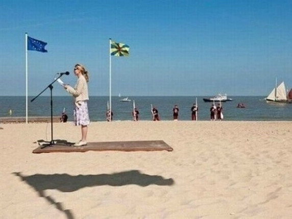 Bóng nắng của lá cờ in trên cát vô tình trùng khớp với bục đứng phát biểu. Điều này khiến cô gái trong bức ảnh như đang bay trên tấm thảm ma thuật.