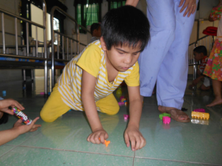 Bé H. bị mù, liệt chân đang bò trên sàn nhà.
