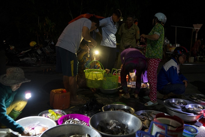Trong tư thế ngồi "chồm hổm", người mua dùng đèn rọi vào chiếc cân đòn để người bán xem số cân, sau đó ai cũng cúi rạp người để kiểm đếm, tính tiền. Ảnh: PNS