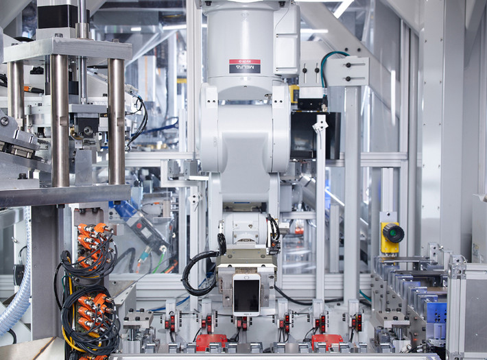 Những cánh tay robot tự động đang di chuyển trái, phải, lên, xuống với độ chính xác và tốc độ cao. Trong khi các kỹ thuật viên trong màu áo phòng thí nghiệm xanh, đeo kính an toàn và găng tay giám sát từng công đoạn được thực hiện bởi những cánh tay robot.