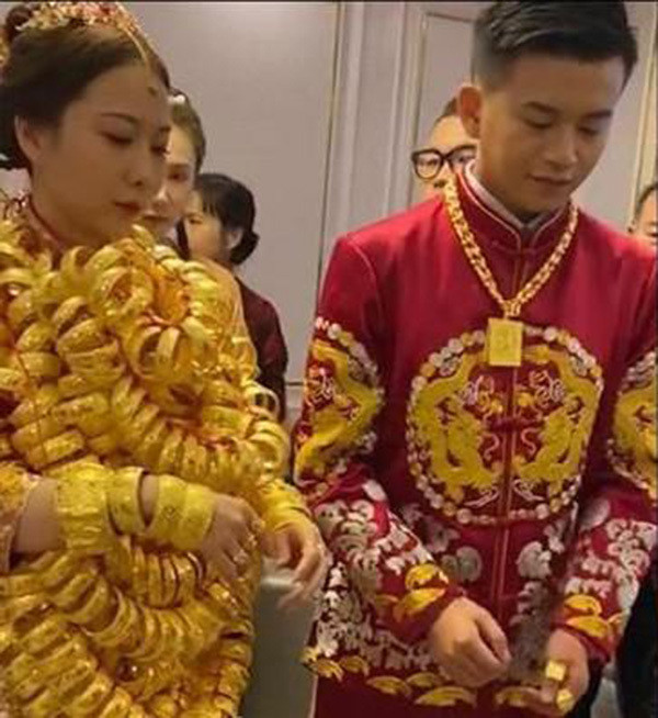 Cặp vợ chồng trẻ diện trang phục cưới truyền thống màu đỏ vô cùng lộng lẫy, nổi bật. Điều khiến dân mạng chú ý chính là những chiếc vòng vàng được nối lại đeo trên người cô dâu.