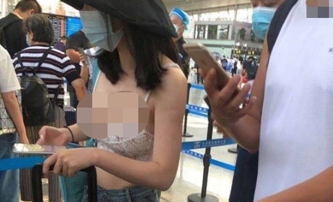 Cô gái "giấu mặt" tự tin, khoe cá tính với chiếc áo ngực mỏng dính, mặc đứng trước quầy check-in ở sân bay.