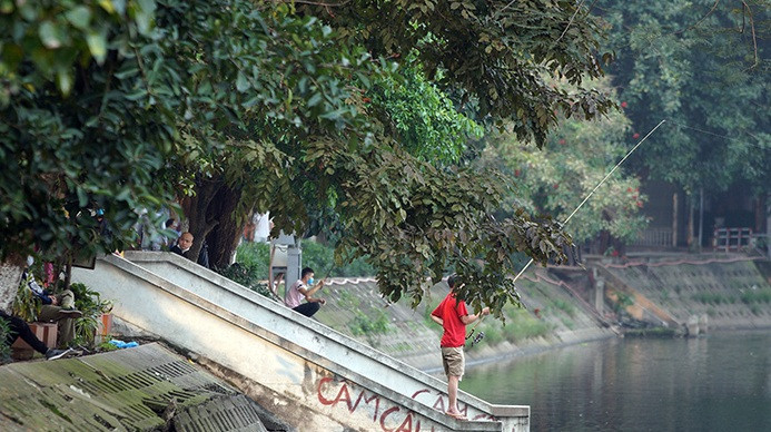 Một người câu cá ở hồ Nam Đồng (phía đường Hồ Đắc Di) cách chốt công an phường Nam Đồng đang phát loa kêu gọi mọi người cách ly ở nhà không xa (ảnh chụp chiều 9/4)