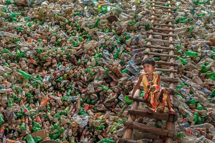 Bức ảnh có tên "Confined in plastic", miêu tả đứa trẻ ngồi trên chiếc thang bên trong nhà máy tái chế rác thải nhựa ở Chittagong, Bangladesh. Tái chế rác thải nhựa là ngành công nghiệp đang nở rộ ở Bangladesh, nhưng công đoạn thu gom và phân loại vẫn tiến hành bằng tay. Ảnh: Subrata Dey.