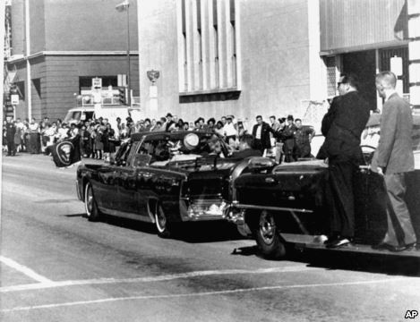 Chiếc xe limousine chở vợ chồng Tổng thống Kennedy đi vào thành phố Dallas, Texas. Chiếc xe theo sau chở nhân viên mật vụ đi theo bảo vệ Tổng thống Kennydy.