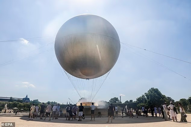 Người dân tránh nắng phía dưới khinh khí cầu treo vạc giữ lửa Olympic tại Vườn Tuileries ở Paris, Pháp. Ảnh: EPA.