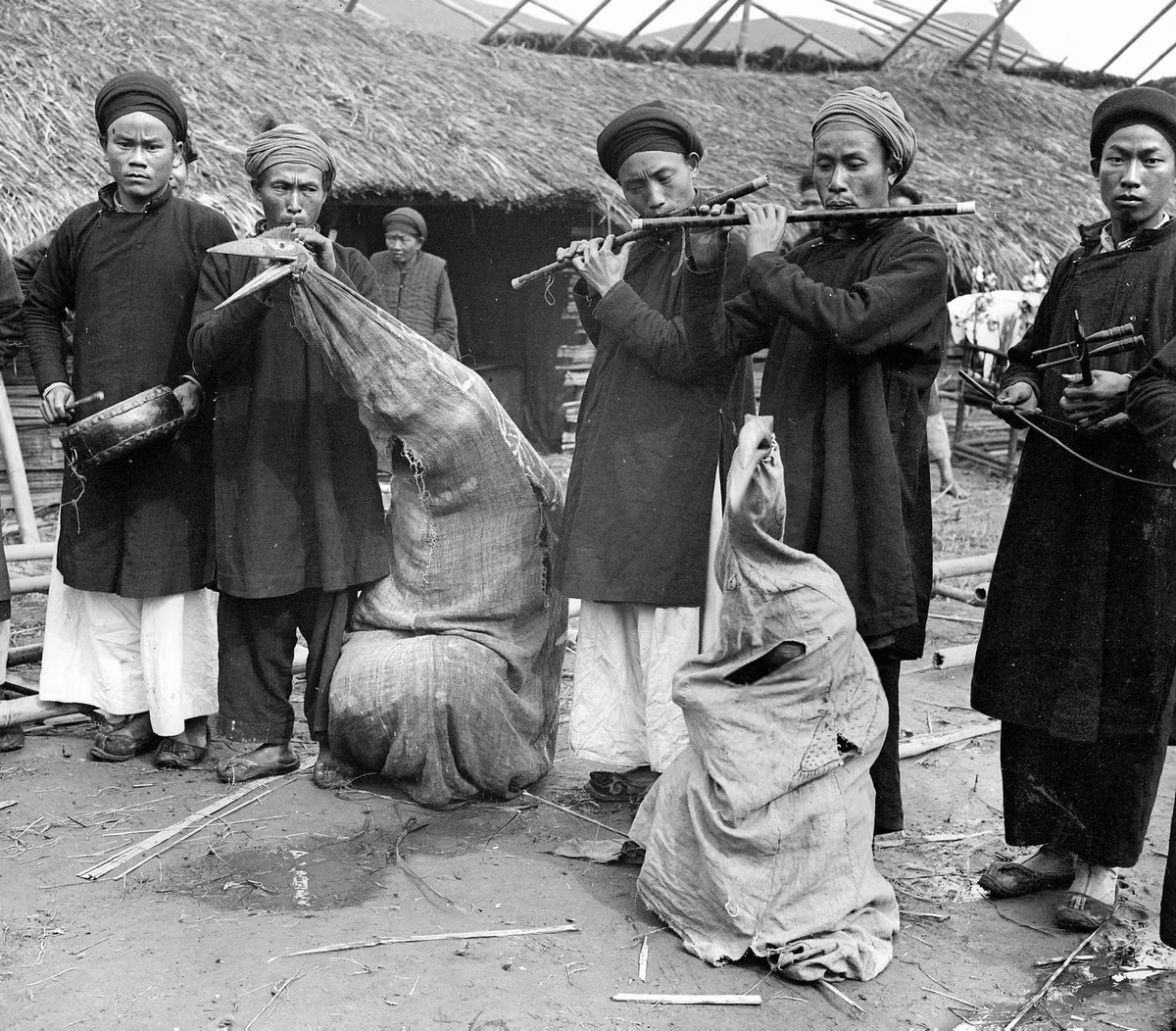 Các nhạc công đánh trống, thổi kèn, kéo đàn trong một đám tang ở Bảo Lạc, Cao Bằng năm 1902. Hai người hóa trang thành chim thần theo phong tục địa phương. Ảnh: LL/Roger Viollet via Getty Images.