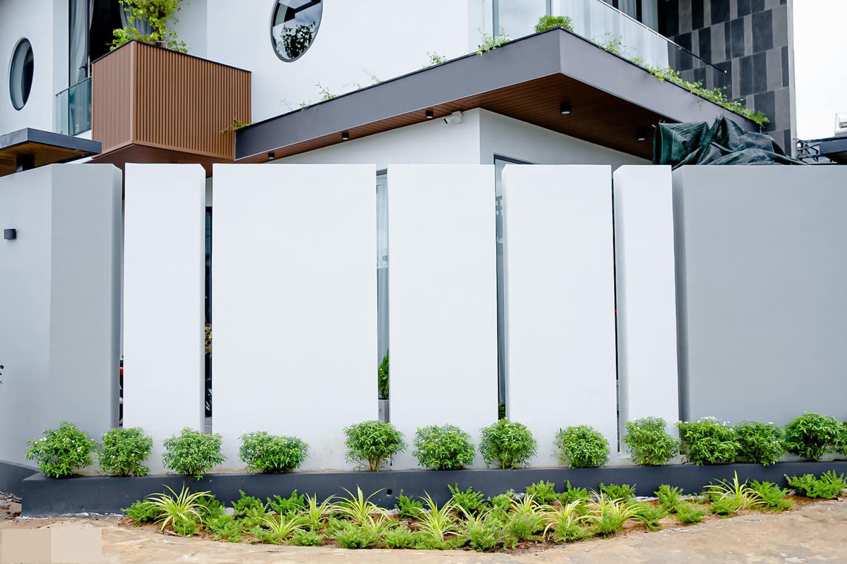 Mặt tiền và ngoại cảnh được chăm chút tỉ mỉ. Phần hiên nhà và hành lang ốp lam gỗ nhựa màu nâu vàng làm điểm nhấn. Những khung cửa tròn lấy sáng phảng phất chút truyền thống nhưng không làm mất đi sự trẻ trung của công trình. Cây xanh đưa đến cảm giác mát mẻ, trong lành.