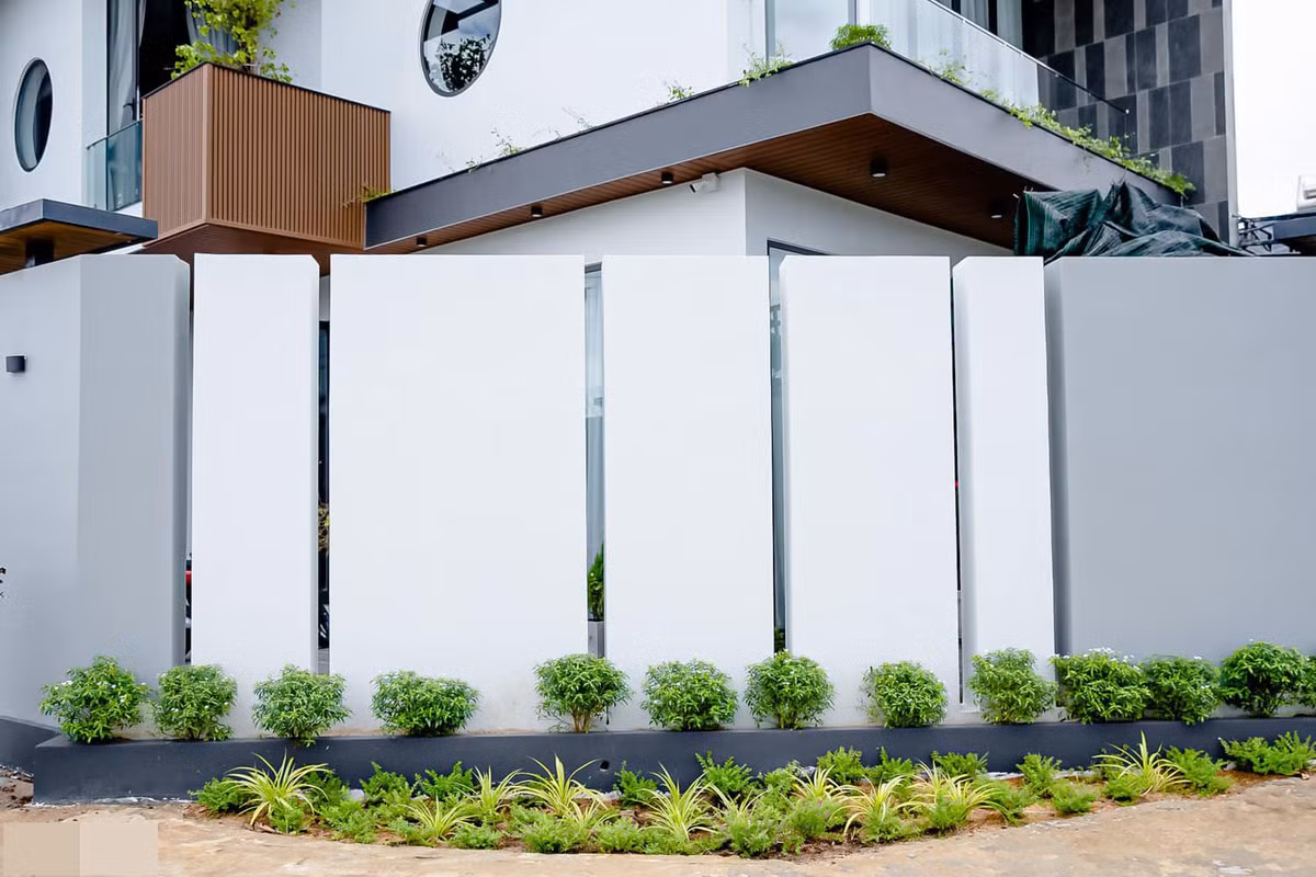 Mặt tiền và ngoại cảnh được chăm chút tỉ mỉ. Phần hiên nhà và hành lang ốp lam gỗ nhựa màu nâu vàng làm điểm nhấn. Những khung cửa tròn lấy sáng phảng phất chút truyền thống nhưng không làm mất đi sự trẻ trung của công trình. Cây xanh đưa đến cảm giác mát mẻ, trong lành.