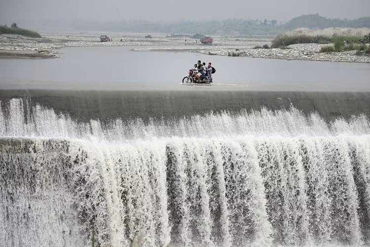 Liều mạng dùng xe máy chở con cái đi qua một con đập bị tràn nước gần thị trấn Pengzhou, tỉnh Tứ Xuyên, Trung Quốc.