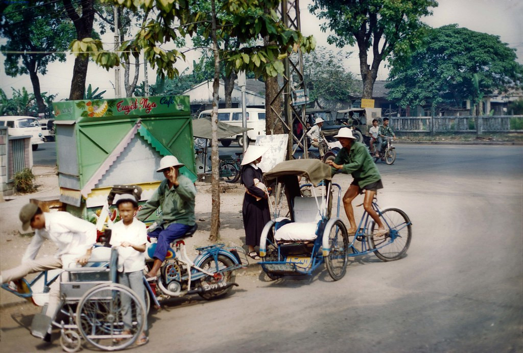 Một chiếc xích lô ở ngã tư Nguyễn Tri Phương - Trần Quốc Toản, Sài Gòn 1971. Cạnh đó là một xích lô máy và xe lăn. Ảnh: Mike Roche.