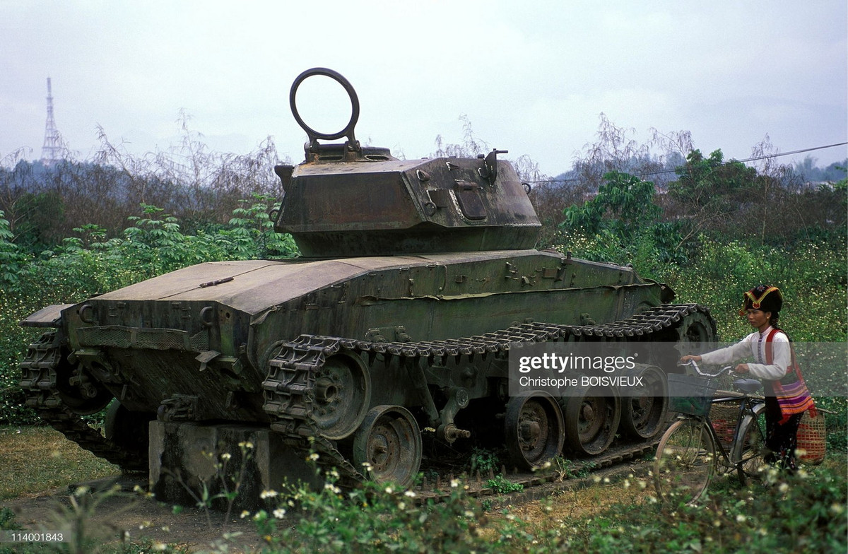 Người phụ nữ dân tộc Thái dắt xe đạp đi ngang qua chiếc xe tăng đã ngừng hoạt động nửa thế kỷ.