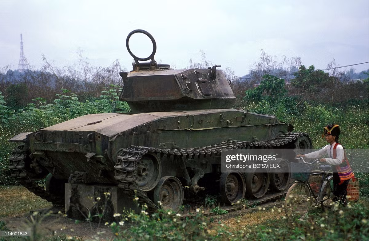 Người phụ nữ dân tộc Thái dắt xe đạp đi ngang qua chiếc xe tăng đã ngừng hoạt động nửa thế kỷ.