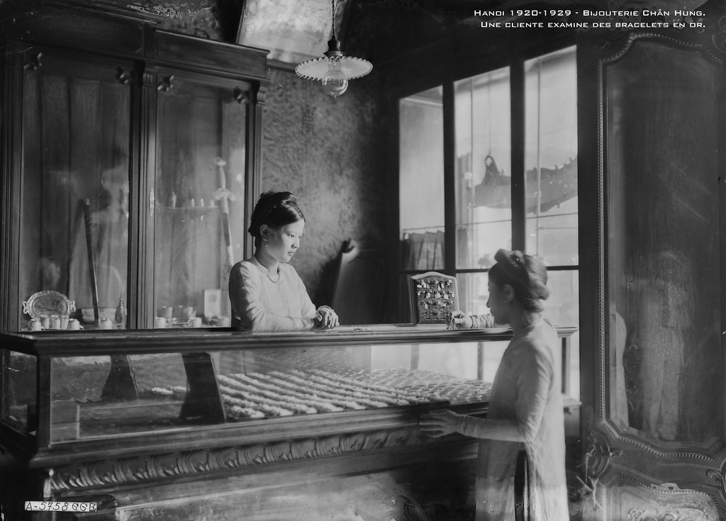 Một khách hàng đang xem xét các vòng đeo tay bằng vàng tại hiệu vàng bạc Chân Hưng trên phố Hàng Bạc, thập niên 1920.