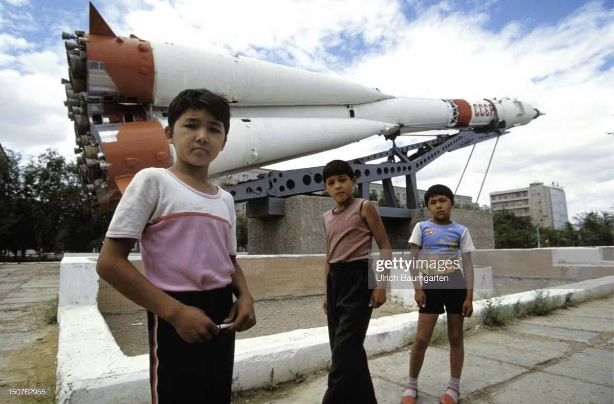 Những đứa trẻ đứng trước đài kỷ niệm tên lửa Soyuz của Liên Xô. Kazakhstan là nơi có sân bay vũ trụ Baykonur, sân bay vũ trụ đầu tiên và lớn nhất trên thế giới do Liên Xô xây dựng.