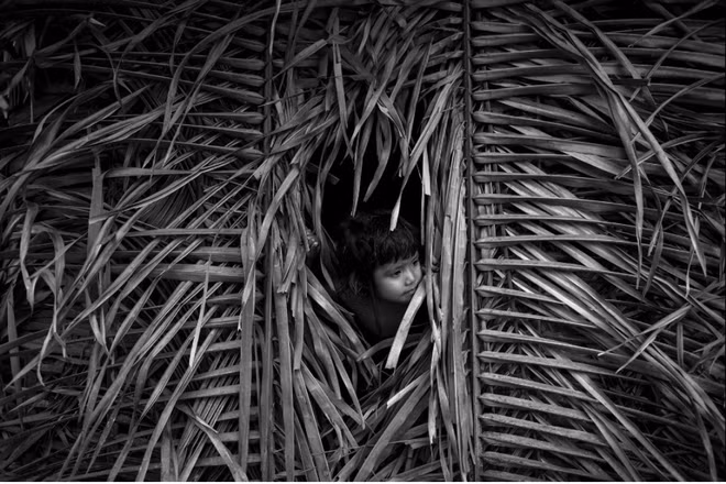 Một đứa trẻ Awa đứng bên trong "nhà" lợp bằng lá khô.