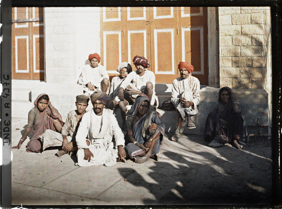 Một nhóm nam và nữ giới ngồi trước hiên một tòa nhà.