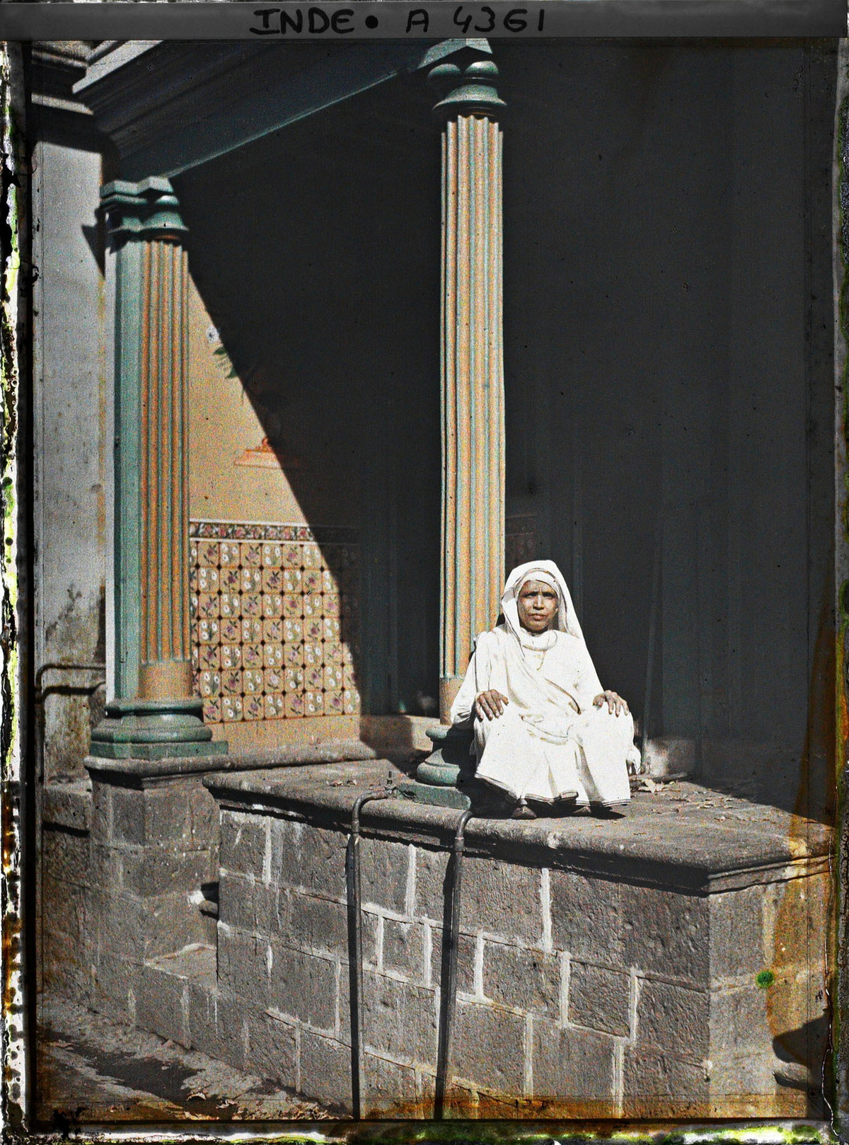 Cụ bà mặc đồ trắng ngồi trên hiên nhà.