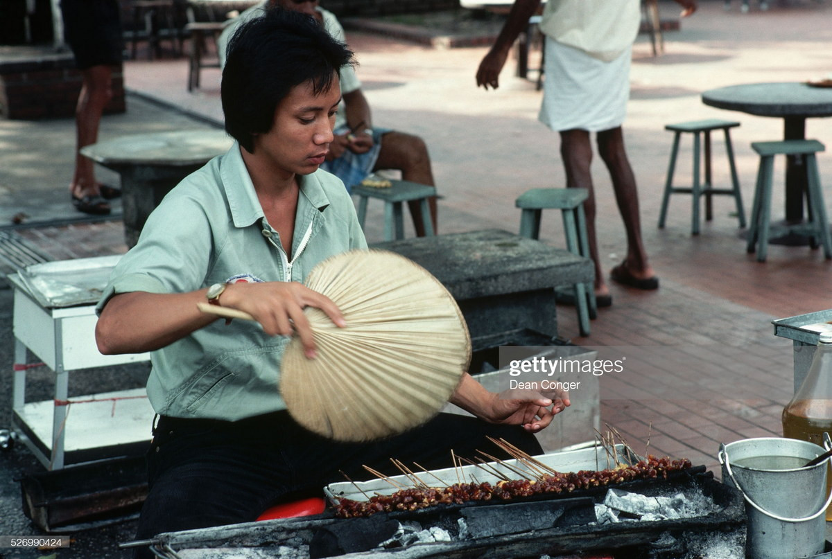 Người phụ nữ quạt chả nướng satay tại quán ăn đường phố Singapore.