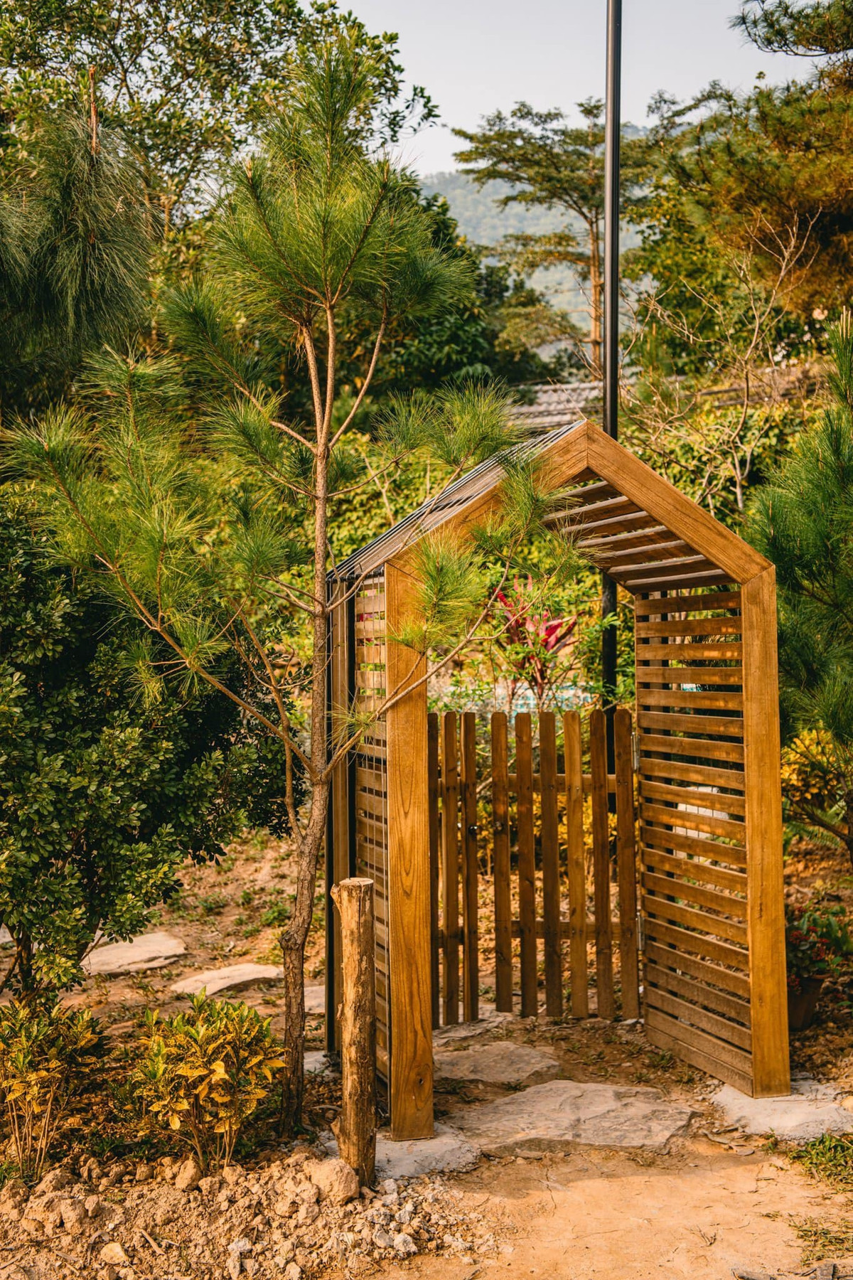 Gia chủ là người hay đi du lịch nên mong muốn có nơi chốn nghỉ dưỡng an bình cho cả gia đình. Vì vậy, anh quyết định làm trên mảnh đất của bố để lại một ngôi nhà nhỏ nhắn nhưng đầy đủ tiện nghi. Cổng vào và hiên nhà bằng gỗ màu vàng ấm. Cây mận trước hiên sẽ nở rộ khi vào mùa - một màu trắng tinh khôi, ngọt ngào. 