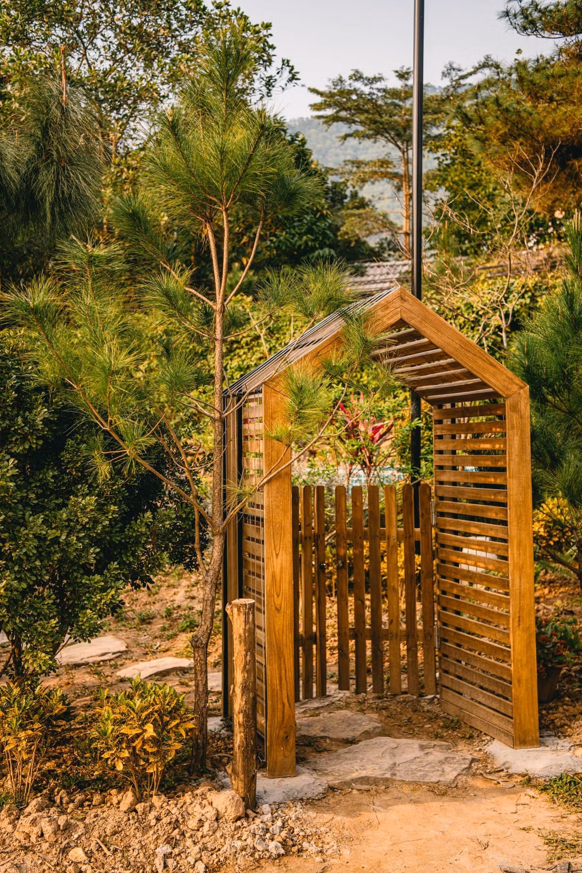 Gia chủ là người hay đi du lịch nên mong muốn có nơi chốn nghỉ dưỡng an bình cho cả gia đình. Vì vậy, anh quyết định làm trên mảnh đất của bố để lại một ngôi nhà nhỏ nhắn nhưng đầy đủ tiện nghi. Cổng vào và hiên nhà bằng gỗ màu vàng ấm. Cây mận trước hiên sẽ nở rộ khi vào mùa - một màu trắng tinh khôi, ngọt ngào. 