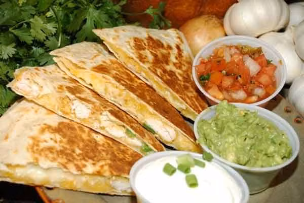 2. Quesadillas. Chỉ cần kẹp pho mát với vỏ bánh ngô rồi nướng trên bếp lửa là bạn đã ngay món bánh quesadilla. Tuy nhiên tại các nhà hàng hay các quầy hàng vỉa hè ở Mexico, quesadillas còn được kèm thêm rất nhiều nhân và gia vị khác (ngoài pho mát) như xúc xích lợn, nấm, tỏi, đậu, da lợn chiên, thịt gà hầm... rồi chiên lên hoặc nướng trên than. Ngoài lớp vỏ được làm từ các loại ngô thông thường, một số nơi còn biến tấu nguyên liệu vỏ bánh bằng các loại bột ngô có pha thêm nguyên liệu khác để cho đời loại quesadillas nhiều màu sắc hơn.