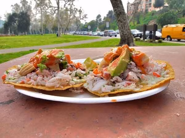 4. Tostadas. Nguồn gốc ra đời của tostadas là để tận dụng bánh bột ngô đã cũ, không còn đủ mềm để cuộn lại thành tacos, nhưng vẫn còn ăn được. Bánh ngô cũ được rán trong dầu sôi cho đến khi trở nên vàng, cứng và giòn. Để món vỏ bánh thêm hấp dẫn, người Mexico nghĩ ra việc phủ lên bề mặt của bánh một lớp nhân bao gồm đậu, thịt gà, kem, rau diếp thái nhỏ, hành tây, bơ và pho mát tươi.