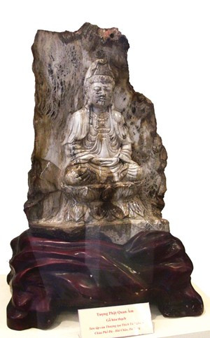Pho tượng Phật đồng đen thế kỷ thứ X mang đặc điểm văn hóa Chăm. Đây là bức tượng làm người xem suy nghĩ và liên tưởng rất nhiều đến tượng Phật Bà (đã được xác nhận là bảo vật quốc gia) đang lưu giữ tại Bảo tàng Chăm. Cả hai pho tượng Phật Bà đều cùng phong cách để trần nửa phía trên, cùng loại chất liệu đồng đen. Và bức tượng đang triển lãm còn có niên đại trước pho tượng đang là bảo vật quốc gia 200 năm. Ảnh: Tượng Phật Quan Âm (gỗ hóa thạch).
