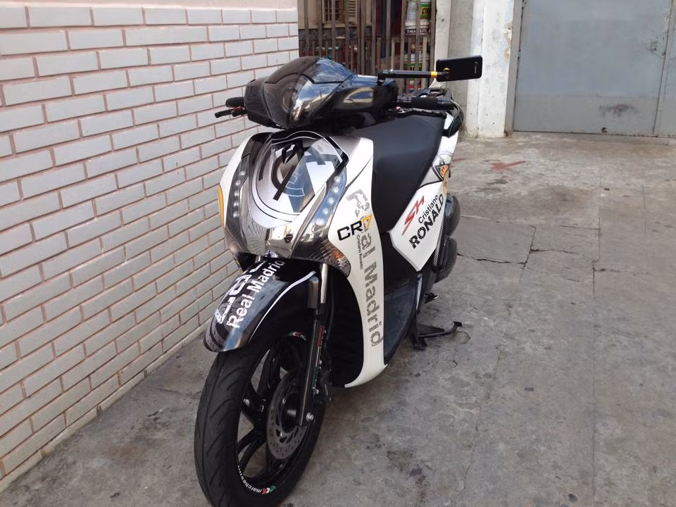 Chiếc xe độ mới toanh của fan cuồng này là sự kết hợp hài hòa giữa 2 gam màu tương phản đen trắng cùng dàn tem Real Madrid. Logo của câu lạc bộ nổi bật trên mặt nạ và dè trước của xe.