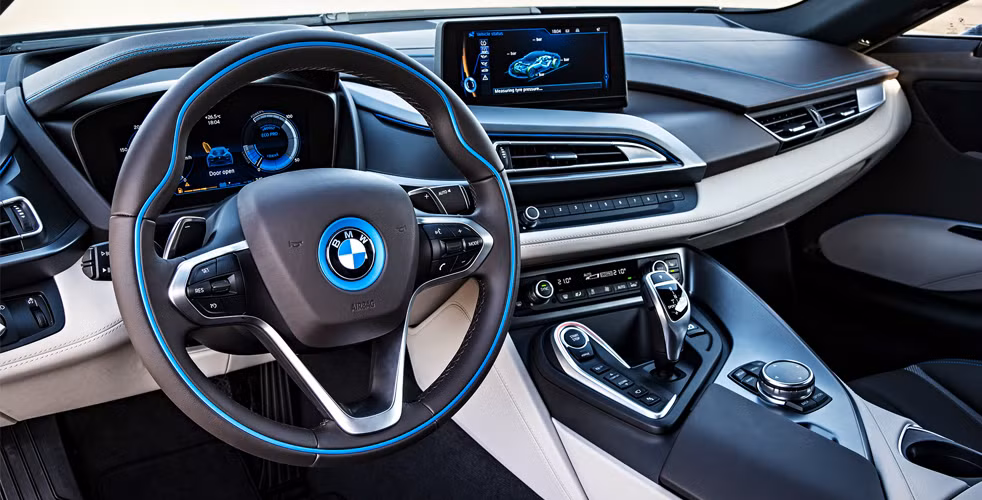 Vô-lăng của BMW i8 mang đậm dấu ấn thiết kế của dòng xe BMW i-Series. Mép vô-lăng được viền gỗ và biểu tượng của BMW được bao quanh bởi vòng tròn màu xanh. Đây là chiếc vô-lăng nhẹ nhất trong tất cả các dòng xe mà BMW từng sản xuất. Trong khi đó, bảng táp-lô được tích hợp màn hình hiển thị có kích thước 8.8 inch hiển thị thông tin của xe và các chế độ lái tương ứng.