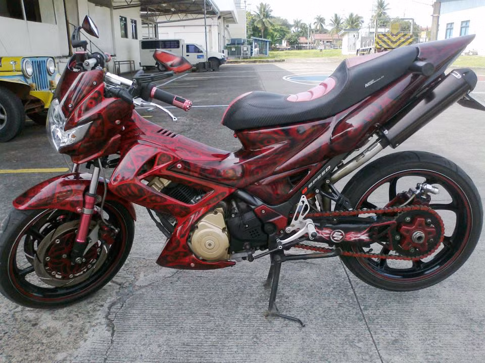 Nhiều tín đồ đam mê Suzuki Raider 150 phải thốt lên rằng đây là một phiên bản độ tuyệt đẹp và đầy uy lực. Xe được trang bị 2 ống pô hầm hố cho tiếng thét kinh hoàng, đi cùng dàn áo Airbrush họa tiết đỏ thẫm đầy ma mị.